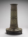 A cylindrical brass stand with ornate incised designs