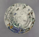 A ceramic plate with a design of plants, insects and a spider web.
