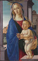 A woman holds a baby in front of a background of buildings.