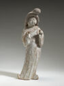 An earthenware figure of a standing woman wearing long, draped robes. Her face is plump and her hair sits on top of her head in rounded shapes.