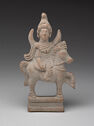 A terracotta sculpture of a person decorated with a hat and shoulder armor riding a standing horse. It is on a small platform and is grey in color.