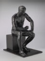 A nude statue of a man seated, resting his right arm on his knee.