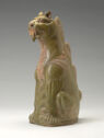 A led-glazed ware figure of a seated lion-like creature. It sits on its hind legs and is colored a medium-green with tan detailing. It has protruding teeth and spikes going up its back.