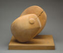 A wooden sculpture of a partially divided ovoid form with a blunt, rounded end on a flat wooden base.