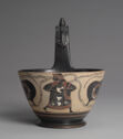 A bowl with a large handle and a figure on it. 
