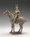 An earthenware figurine of a man riding a horse. The man wears a tall, detailed hat and a pointed, wrapped jacket. The horse is facing the left of the viewer and its hooves are all on a small plinthe.