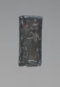 An intaglio black, hematite object in the shape of a cylinder. It is engraved with an image of a standing person wearing a long skirt and a headpiece and a small bird next to them. There are other engravings that wrap around the sides.