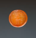 A carved orange agate disk with the image of a standing stag on it. The stag has large horns and a neck-tie that sticks outward. There are small lines and a thick lip along the edge.