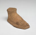 A terracotta sculpture in the shape of a flat right foot. It is cut off above the ankle and the toes are long. It is colored pale orange with black and grey specks throughout.