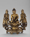 A gilt bronze sculpture of a man seated with two smaller people standing by his side on a decorated pedestal.