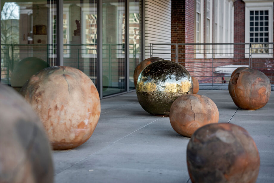 A grouping of terracotta spheres of varying sizes displayed on an outdoor concrete terrace.