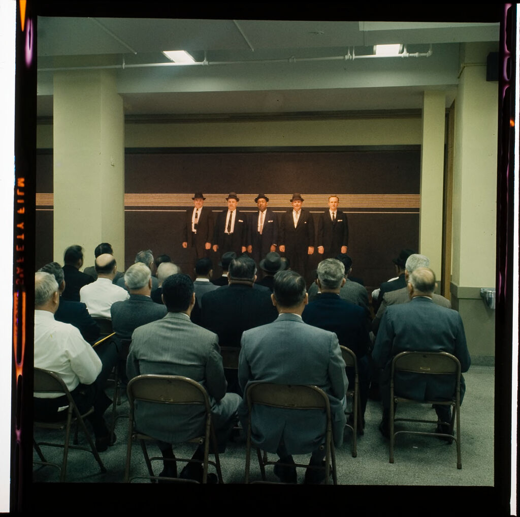 Untitled (Men In Suits Standing In Police Line-Up, Audience Watching)