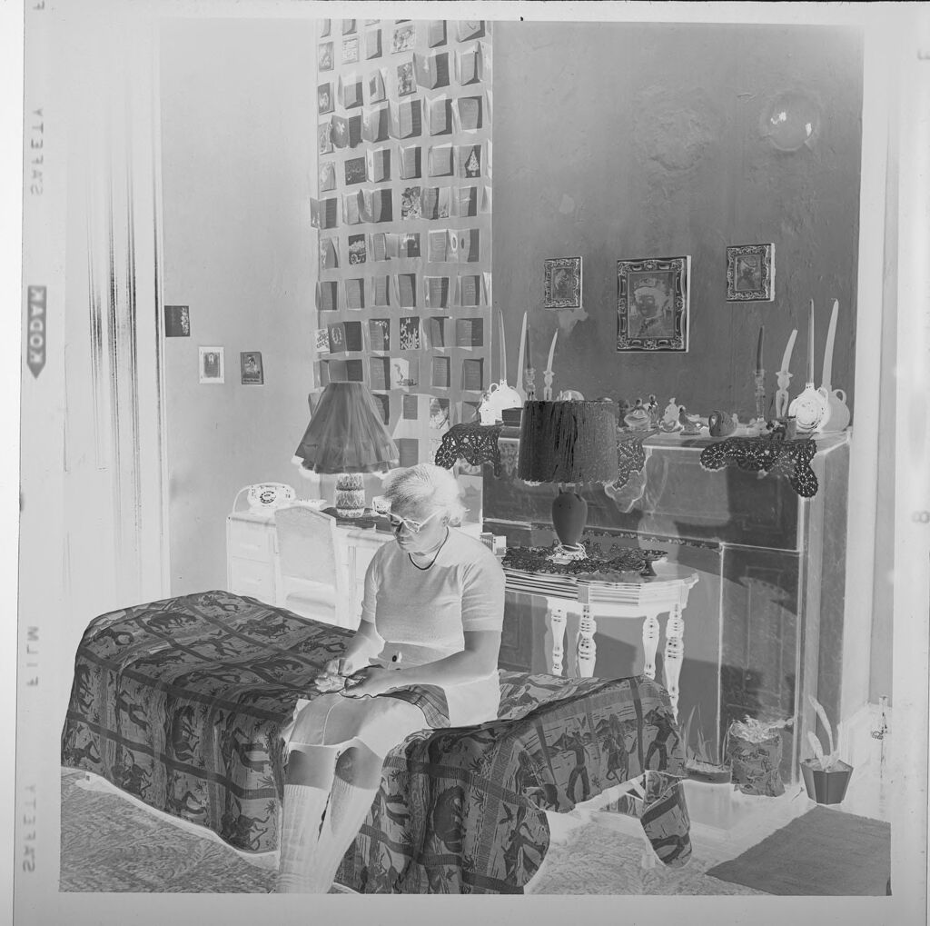 Untitled (Woman Sitting On Bed Inside Small House, Looking Down)