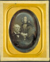 Formal portrait of a couple, a woman stands next to a seated man on the left.
