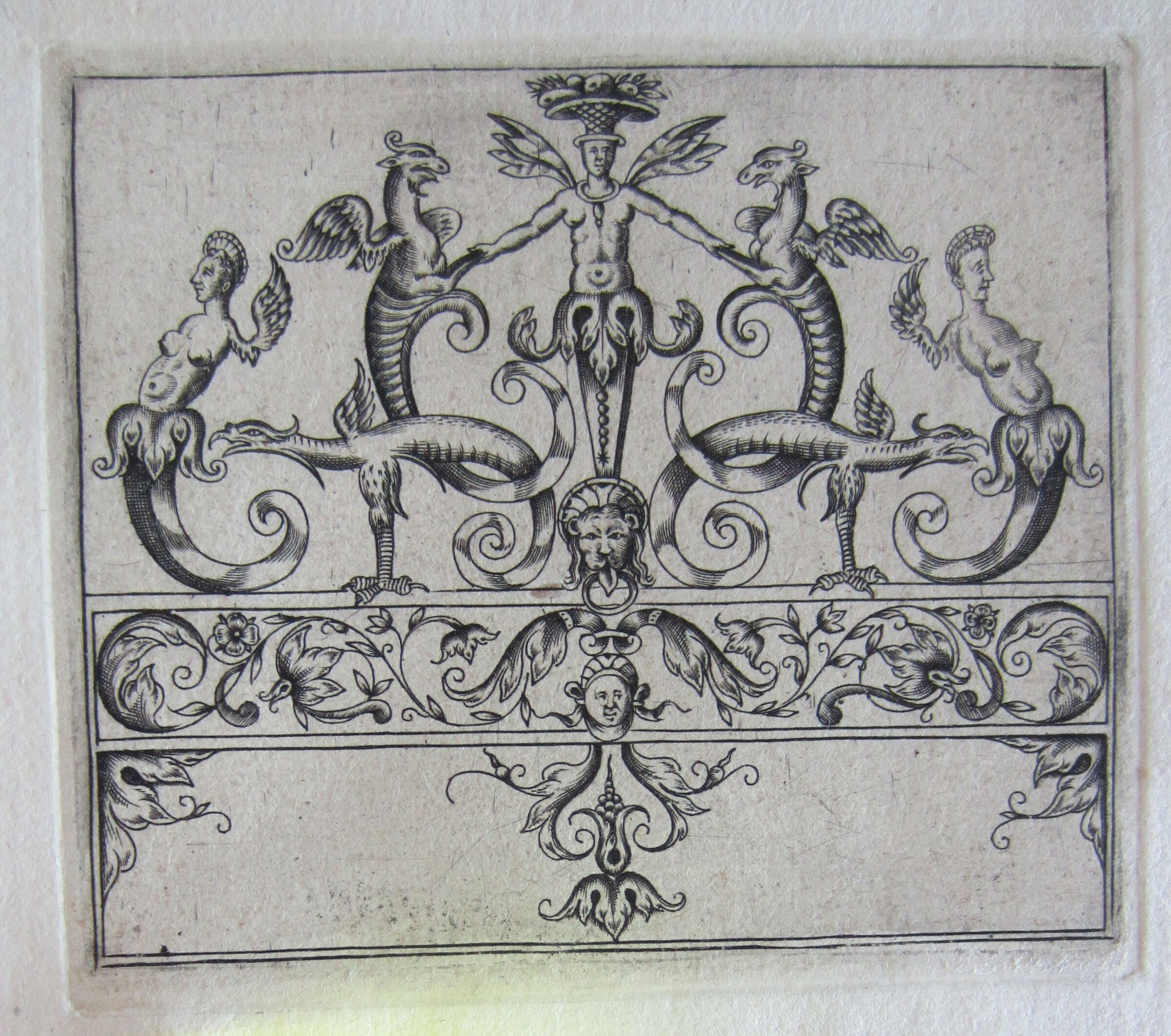 Tripartite Ornament With A Central Leonine Mask Holding A Ring In Its Mouth, A Term Bearing A Fruit Basket Above