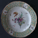 A white plate with a green and yellow rim, featuring four painted bird scenes around the rim. The center has a large bouquet of flowers, with roses and one prominent tulip at the top.