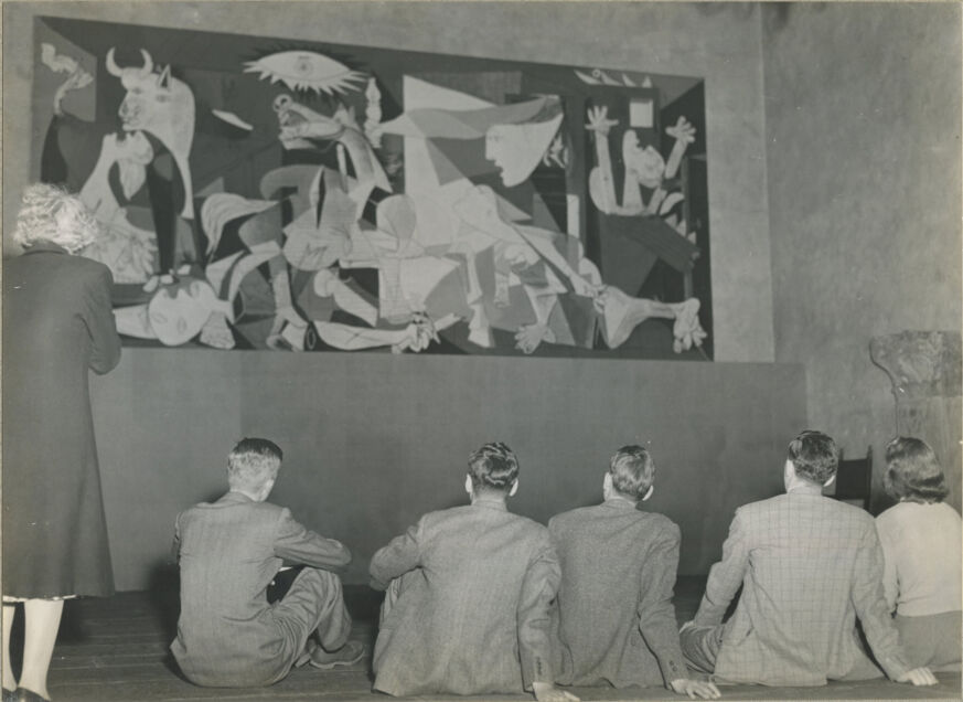 Six students stand or sit in a large gallery in front of a wide abstract painting.