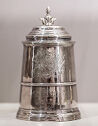 A wide round silver vessel with a decorative handle on the lid.