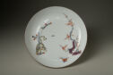 A round white plate wiht painted designs in yellow, blue, red, and purple.