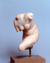 A small marble sculpture depicts a plump female figure with a curved torso and missing head and limbs.