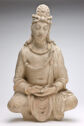 A stucco sculpture of a man sitting cross-legged and wearing a draped robe.