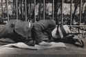 A black and white photograph of a man sleeping on a sidewalk.