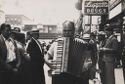 A black and white photograph of man playing the accordion on a city street.