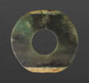 A dark green jade disk with a circle cut out in the middle. There are two small holes at the top.