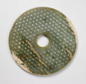 A green jade disk with a circle cut out in the middle. There is a pattern of small relief hexagons throughout the piece.