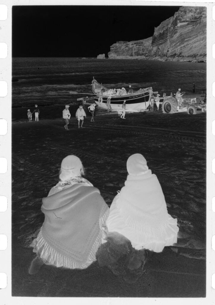 Untitled (Two Woman Sitting On Beach Watching Men Move Rowboat, Nazaré, Portugal)