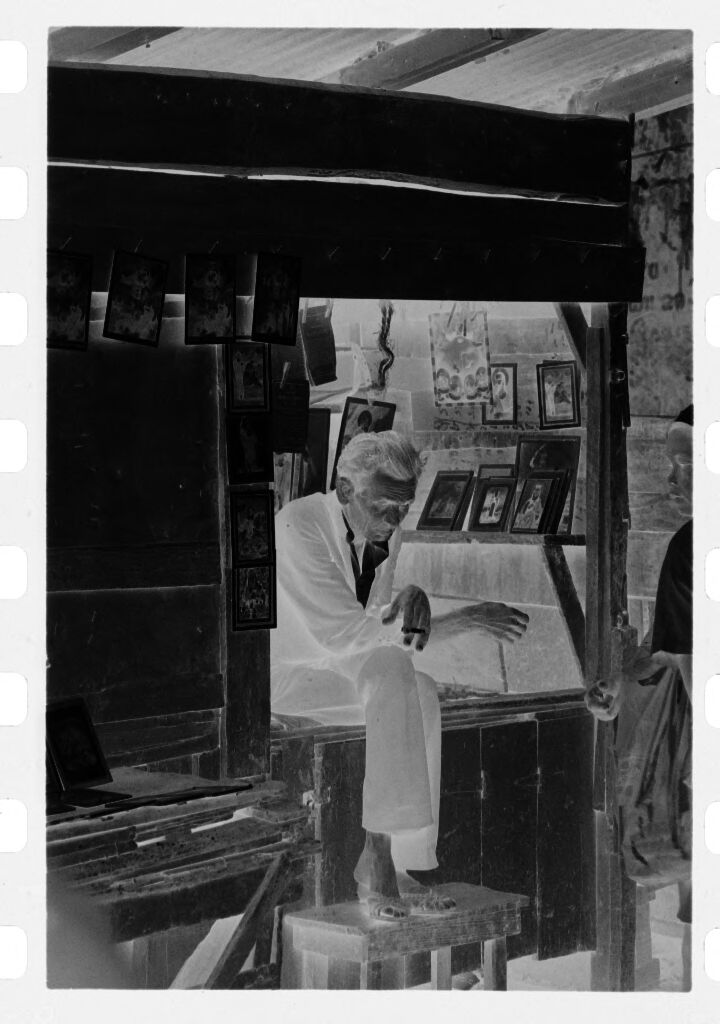 Untitled (Picture Stall In Market With Man Sitting On Counter Smoking Cigarette)