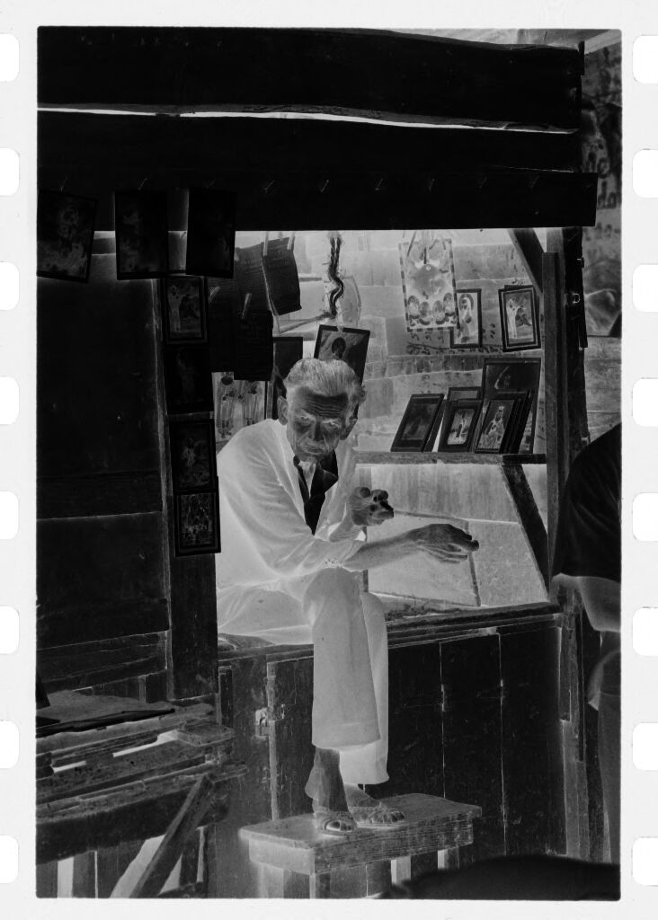 Untitled (Picture Stall In Market With Man Sitting On Counter Smoking Cigarette)