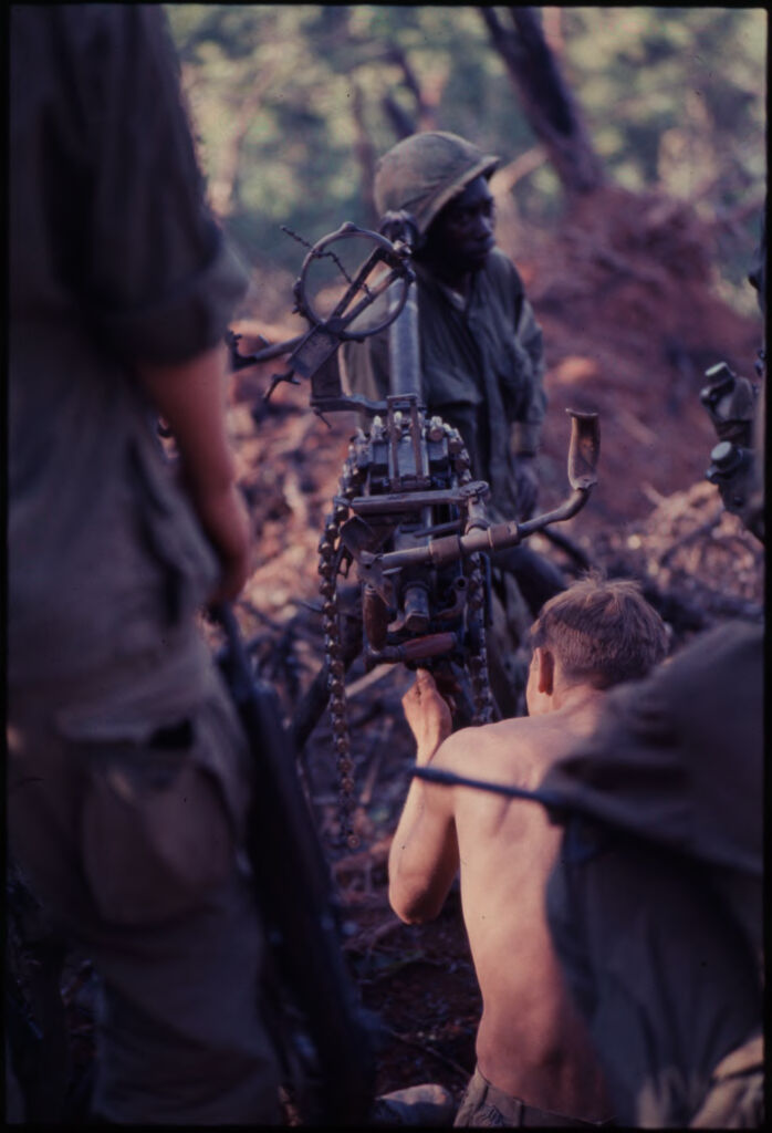 Untitled (Soldier Working On Gear Or Weapon Set Up In Woods, Vietnam)