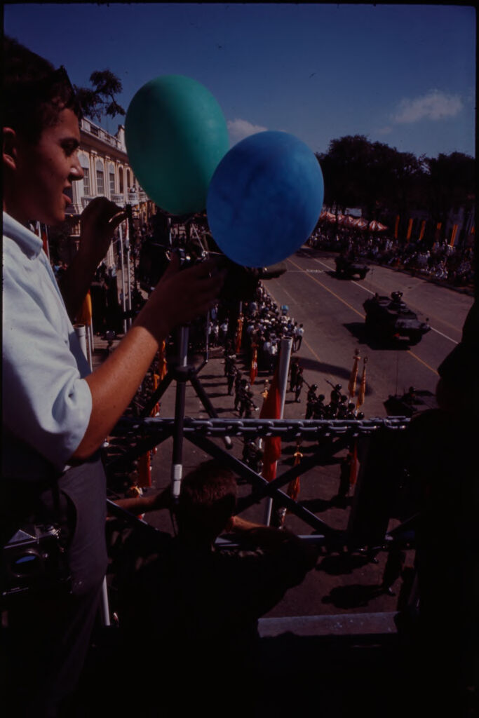 Untitled (Man Holding On To A Blue And A Green Balloon Above Parade Route, Vietnam)