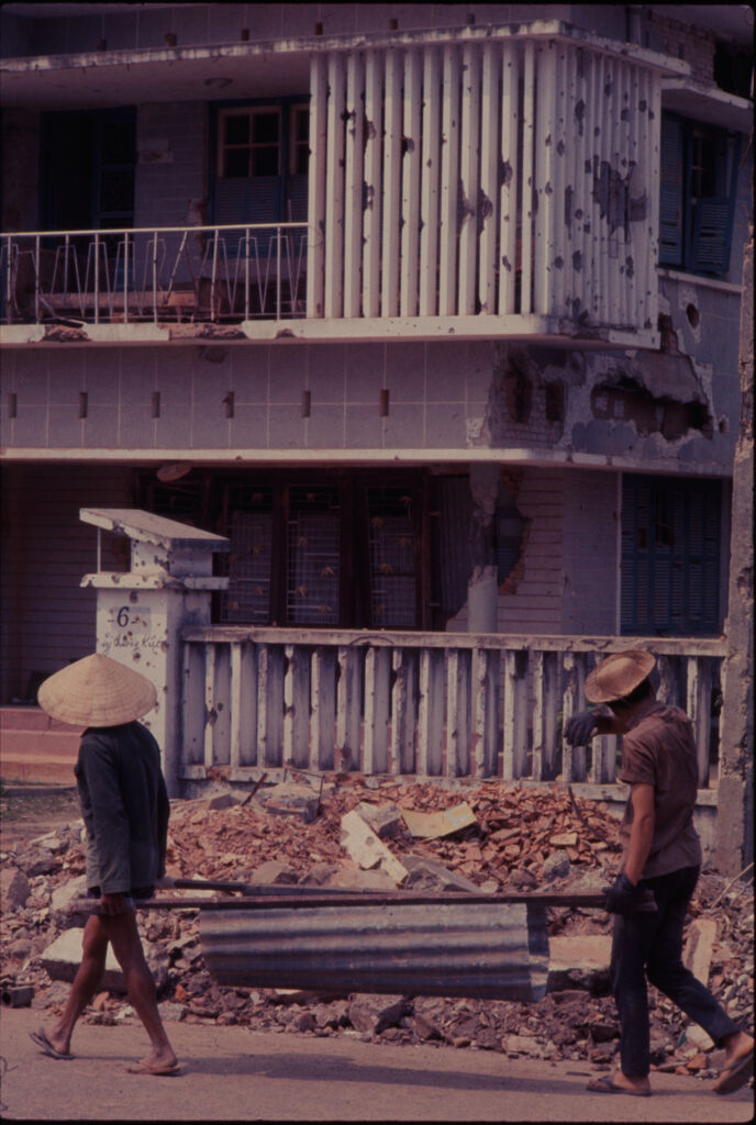 Untitled (Men Carrying Metal Trough Away From Rubble Pile, Hue, Vietnam)