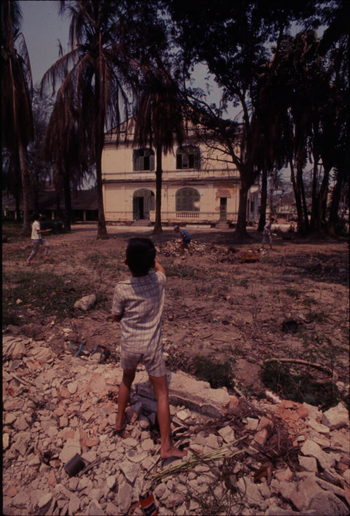 Untitled (Young Boy Throwing Rocks From Rubble Pile Into Field Behind Buildings, Hue, Vietnam)