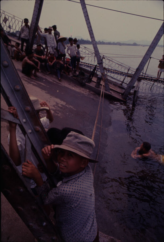 Untitled (Partially Collapsed Bridge Across Perfume River With Young Boy In Foreground Looking At Camera, Hue, Vietnam)