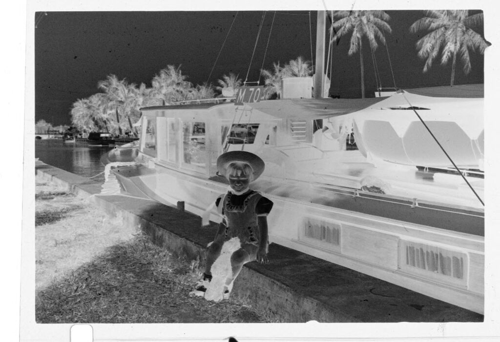 Untitled (Young Girl In Hat Sitting On Ledge In Front Of Boat)