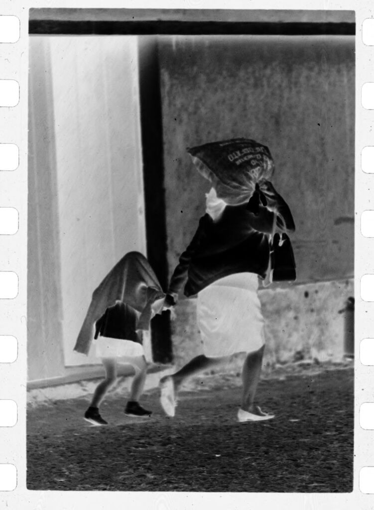 Untitled (Woman Walking Through Street Carrying Sack On Her Shoulder And Holding Young Girl's Hand)