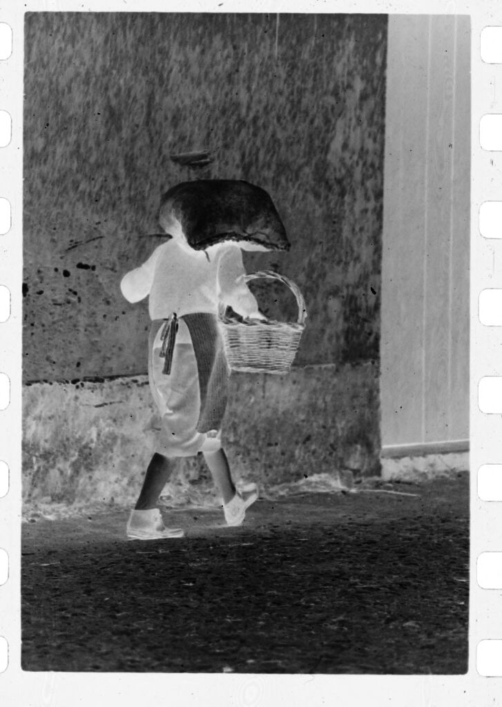 Untitled (Woman Walking Through Street Carrying Sack On Her Head And A Basket)