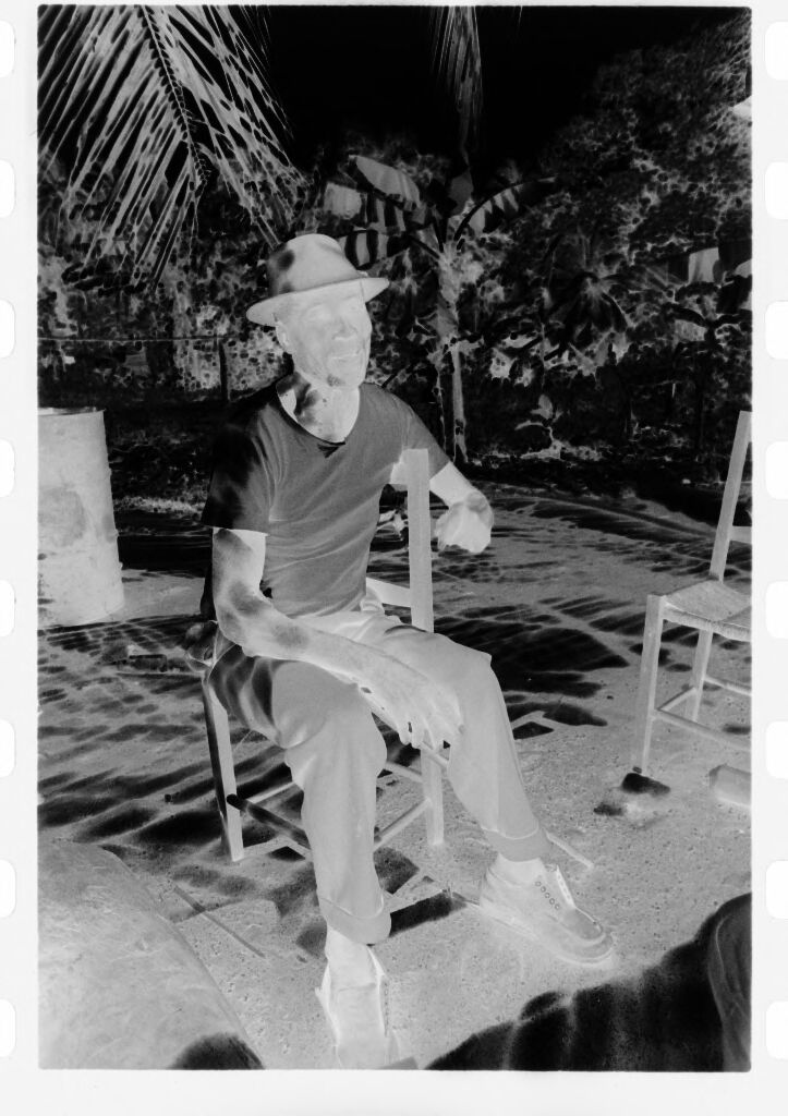 Untitled (Man In White Shirt And Fedora Sitting On Chair Beneath Palm Tree)