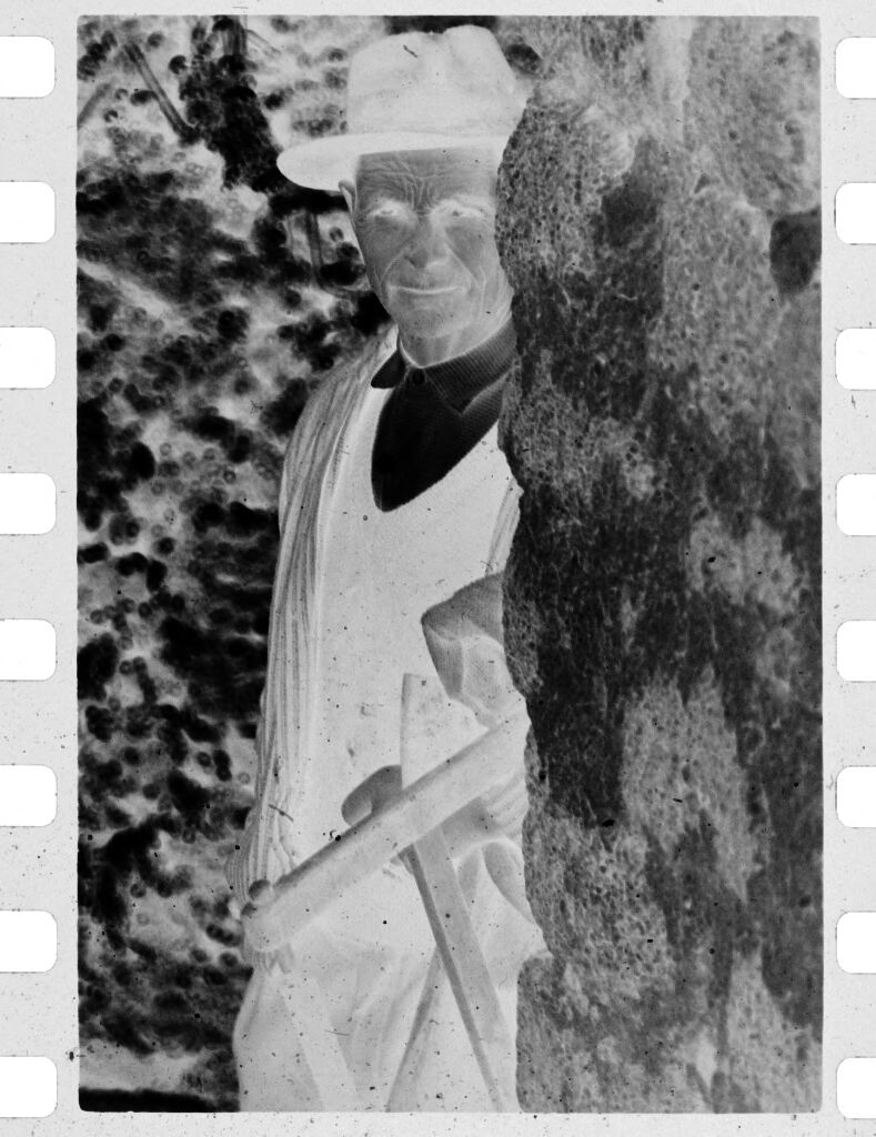 Untitled (Man In Hat Standing Beside Stone Wall)