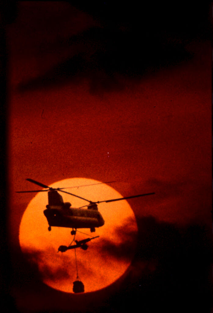 Untitled (Chinook Helicopter Lifting 105Mm Howitzer Silhouetted Against Sun And Low Clouds, Vietnam)