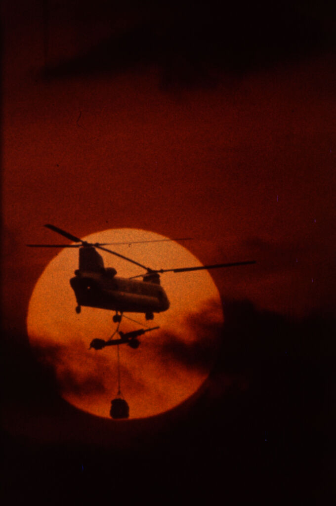 Untitled (Chinook Helicopter Lifting 105Mm Howitzer Silhouetted Against Sun And Low Clouds, Vietnam)