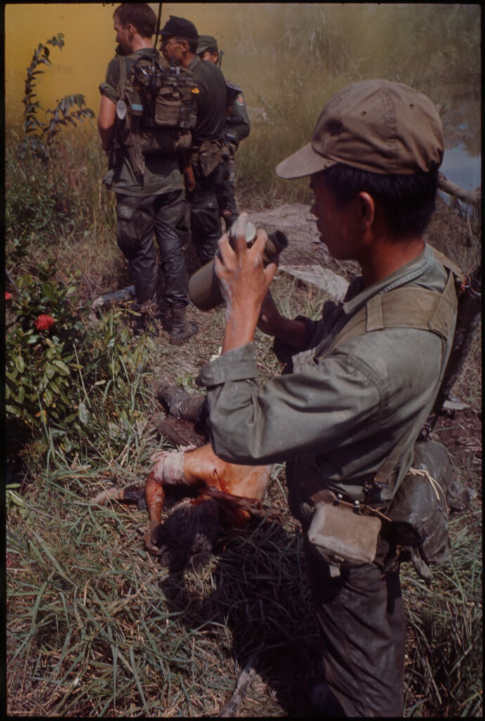 Untitled (Soldiers Standing In Field With Injured Soldier Lying On Ground, Vietnam)