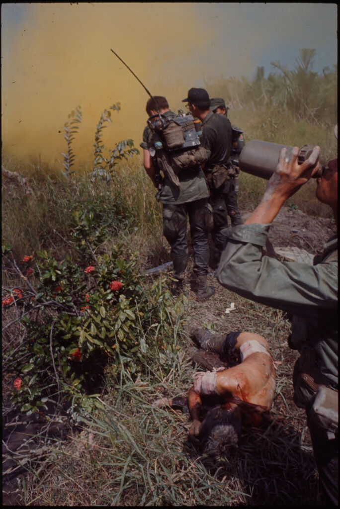 Untitled (Soldiers Standing In Field With Injured Soldier Lying On Ground, Vietnam)