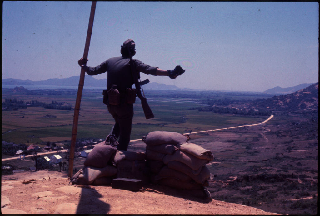 Untitled (Soldier Standing With Flag On Hilltop Overlooking Landscape, Vietnam)