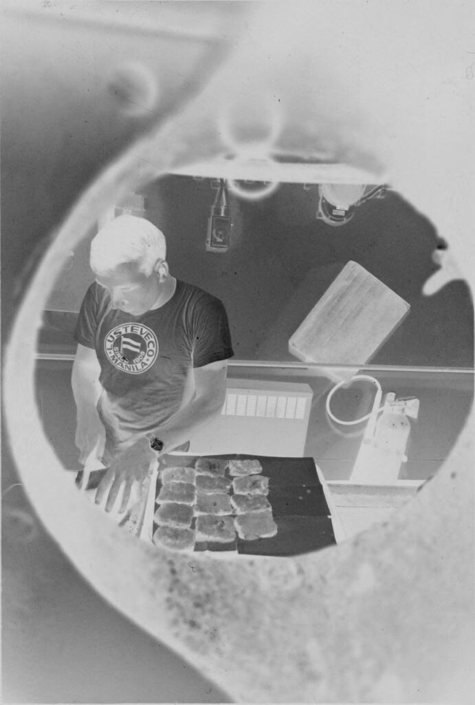 Untitled (View Through Porthole Of Man Cooking In Ship's Kitchen, Vietnam?)
