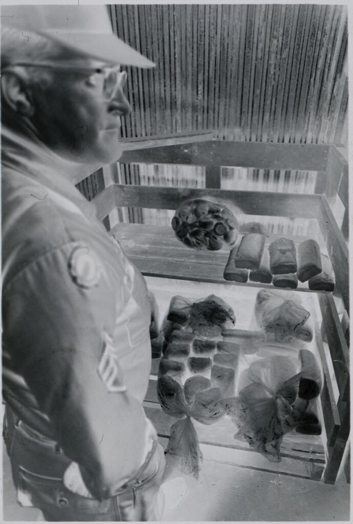 Untitled (Soldier Standing Next To Shelves Holding Bread And Rolls, Vietnam)