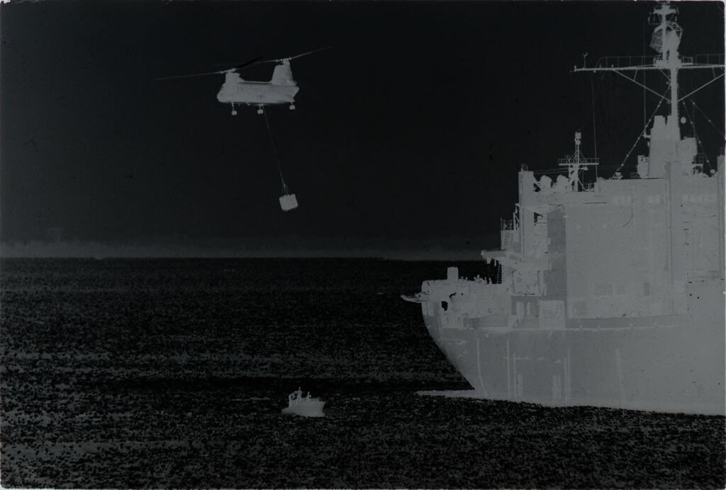 Untitled (Chinook Helicopter Dangling Cargo Hovering Over Small Boat With Soldiers Next To Navy Ship, Vietnam)